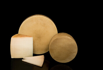 Two cheeses one large and one small isolated on a black background with texture in their rinds next to a wedge and pieces of cheese.