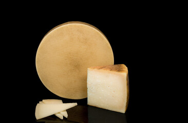 Fototapeta premium A cheese with a texture to its rind isolated on a black background next to a wedge and slices of cheese.