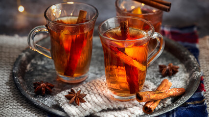 Hot drink for New Year, Christmas or autumn holidays. Mulled cider or spiced punch, tea or mulled white wine with lemon, apples, cinnamon, anise, cloves on a dark background. Banner, no people.