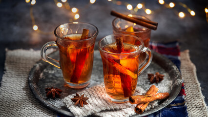 Hot drink for New Year, Christmas or autumn holidays. Mulled cider or spiced punch, tea or mulled white wine with lemon, apples, cinnamon, anise, cloves on a dark background. No People.