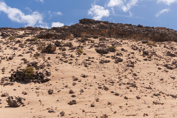 Small and big coastline rocks with many hollows surrounded by dry sandy desert surface, Canary Islands