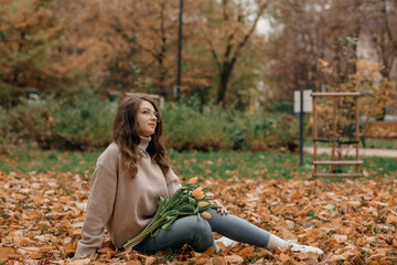 Naklejka na ściany i meble Outdoor photo of glad young lady having fun in autumn park. Young woman with a bouquet of tulips at the autumn park.