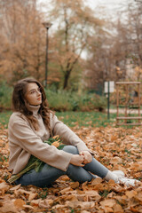 Outdoor photo of glad young lady having fun in autumn park. Young woman with a bouquet of tulips at the autumn park.