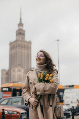 A young girl in glasses with flowers against the background of the Palace of Culture in Warsaw. A...