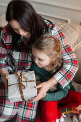 Beautiful mother and daughter in fashionable new year clothes with gifts sit on the sofa on Christmas Eve