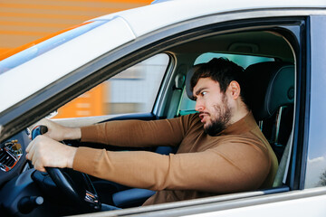 young bearded man at the wheel of a car with bizarre eccentric emotions. males with facially...