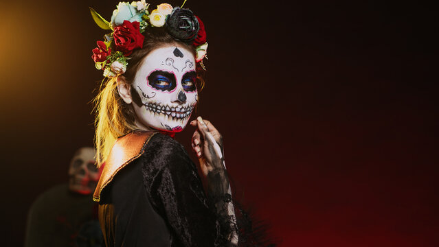 Cavalera catrina luring victims and reaching with hand, tempting and looking flirty on mexican halloween. Lady of death acting horror with skull make up and goddess costume. Handheld shot.