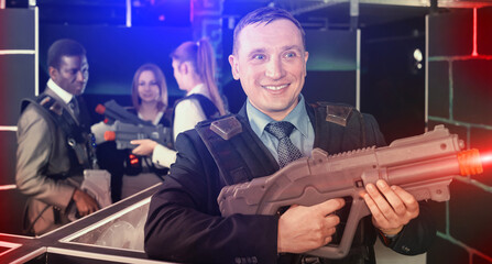 Fototapeta na wymiar Adult man and his colleagues on background having corporative entertainment in laser tag room