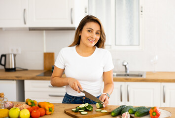 Young smiling woman chopping vegetables in home kitchen, preparing vegan dish
