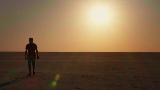 Man walking in deserted places of Africa tawards the sunset making a sign calling to follow. Tourist walking on sand at evening during sunset.