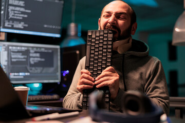 Frustrated programmer wearing cervical neck collar and biting on keyboard, feeling stressed and...