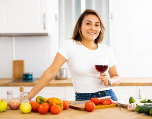 Obraz na płótnie Canvas Happy housewife preparing vegetable salad and drinking red wine