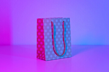 Polka dot paper bag in neon light. The concept of sales, Black Friday, cyber Monday on a blue pink...