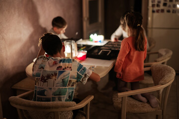 Family spending time together during an energy crisis in Europe causing blackouts. Kids drawing in...
