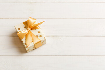 wrapped Christmas or other holiday handmade present in white paper with gold ribbon on colored background. Present box, decoration of gift on colored table, top view with copy space