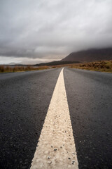 White line on a road leading to mountain in the background. Cloudy sky. Travel and transportation concept.