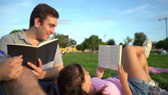 young caucasian woman and man student friends relaxing, having fun, reading and studying in the park