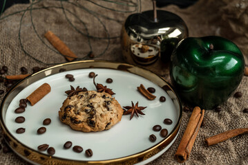 Oatmeal cookies with raisins on a saucer with a gold border. Decorated with decorative apples, cinnamon sticks and anise.