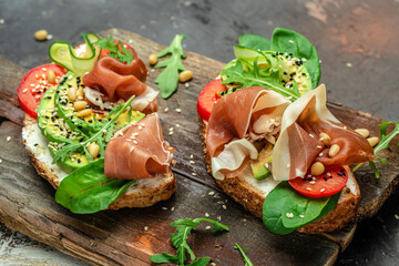 set of sandwich with cream cheese, prosciutto, avocado and fresh greens on a wooden background. Keto breakfast or snack, top view