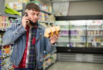 Bearded guy talking on phone advising with someone about purchasing of yogurts in shop
