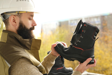 black work boots made of leather with reinforced cape, high top in hands of young bearded man,...