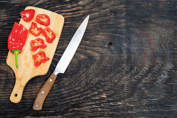 Fresh raw sweet pepper (bell pepper) on a cutting board with a knife. Chopped pepper pieces are...