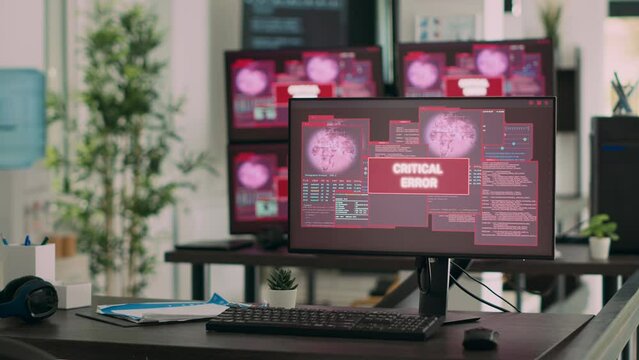 Computers displaying critical error message flashing on screen, dealing with hacking threat and computer malware. Empty desk with multiple monitors showing security breach alert.