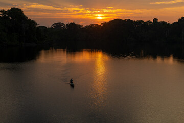 Man silhouette in canoe at sunrise, Amazon rainforest. Amazon river basin in Brazil, Peru, Ecuador,...