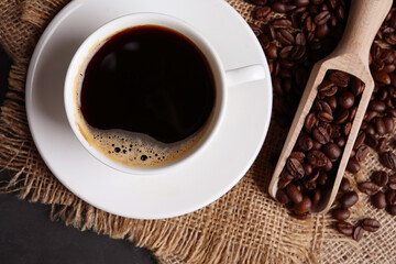 Cup of hot aromatic coffee and scoop with roasted beans on black table, top view