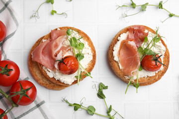 Tasty rusks with prosciutto, cream cheese and tomatoes on white table, flat lay