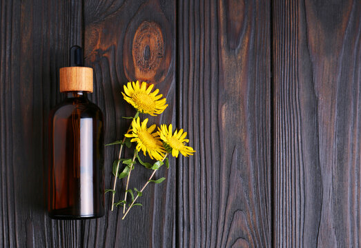 Glass bottle of aromatic essential oil and yellow wildflowers on wooden table, flat lay. Space for text