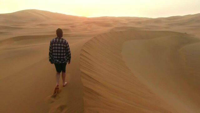 Travel, freedom and desert man walking in dunes of Namibia for adventure, sunset and holiday drone. Peace, explore and vacation with barefoot person in sand of remote landscape with dusk sky horizon.