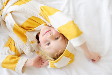 Portrait of cute little child in bathrobe is lying in bed after waking up. Kids clothes for home....