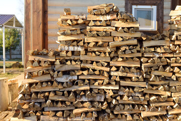 A large woodpile of firewood is stacked in the yard next to the village house. A supply of firewood for the winter.