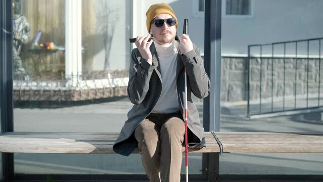 Visually impaired man talking on the phone, sitting on the bench in the city.