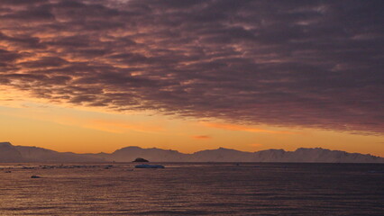 Pink clouds in an orange sky, with mountains and icebergs in silhouette, at Cierva Cove,...