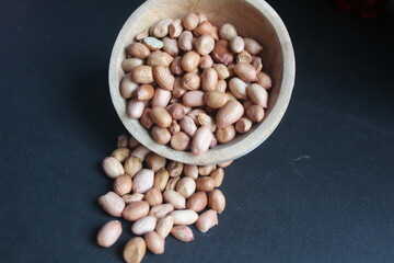 raw peanuts in a wooden bowl on a black background