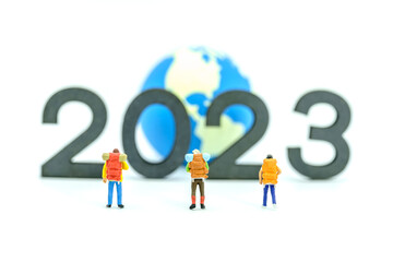 2023 New Year and Travel Concept. Group of traveler miniature figures with backpack standing with wooden number block with mini world ball on white background.