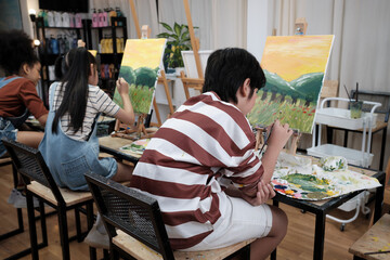 A group of student kids concentrates on acrylic color picture painting with a paintbrush on canvas...