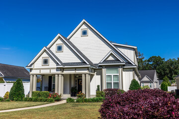 The front view of a cottage craftsman style white house with a triple pitched roof with a sidewalk,...