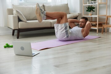 Obraz premium Man sports, watching tape of workout on phone and repeating exercises sports blogger with laptop training online, pumped up man fitness trainer works out at home, the concept of health and body beauty