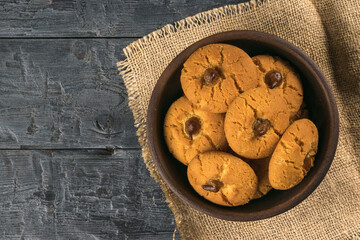 A bowl of cookies on a piece of burlap on a wooden table.