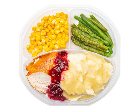 Holiday dinner in a lunch box. Mashed potatoes, turkey, gravy, cranberry sauce, corn, green beans, asparagus. Happy Thanksgiving day. Macro high resolution photo. White isolated background. Food Photo