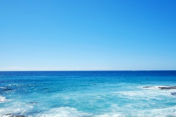 Fototapeta na wymiar Cloudless blue skies and calm waters, waves crashing against the rocks along the Bondi to Bronte coastal walk — Tamarama, Sydney; New South Wales, Australia