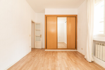 Empty room with a built-in wardrobe with sliding mirror doors combined with wood and a white wooden door and laminated flooring