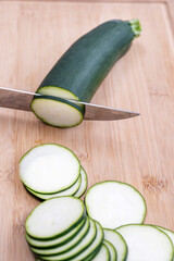 A knife cutting zucchini on a bamboo board