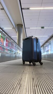 On the passenger conveyor at the airport there is a small blue suitcase that drives forward there is no one around He is alone in a large airport Vacation travel there is space for text