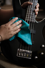 Hands of a man cleaning an electric bass with a microfiber cloth.