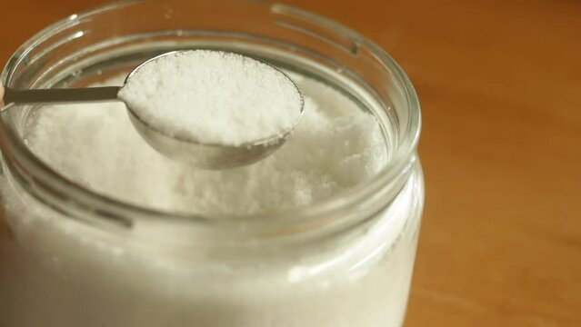 A tablespoon of table sea salt is being scooped with stainless steel measuring spoon cup