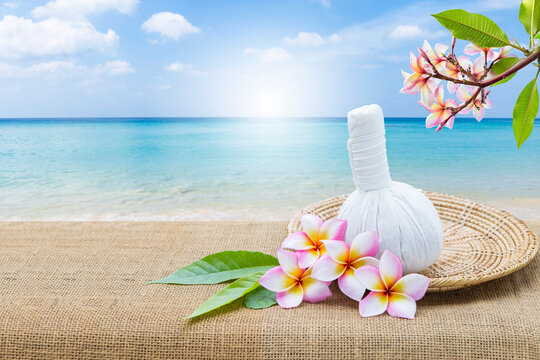 Thai herbs massage ball and plumeria flower in wooden tray over beautiful beach background, spa and wellness concept